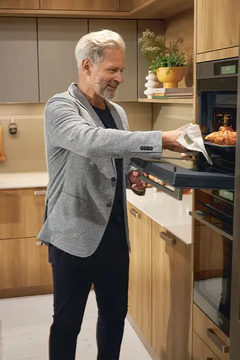 Mann steht vor erhöht eingebautem Backofen in Holzküche.
