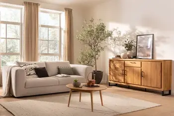 Beiges 2-Sitzer Sofa mit großen bequemen Rückenkissen in einem hellen gemütlichen Wohnzimmer mit Couchtisch und Sideboard aus Massivholz.