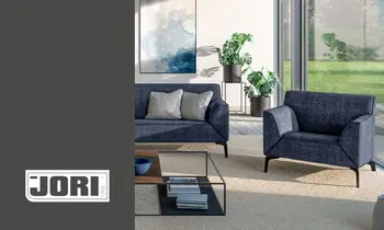 Ein dunkelgraues Sofa der Marke Jori, auf der linken Seite befindet sich das Jori-Logo&nbsp;auf grauem Hintergrund.