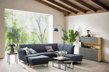 Blaues gemütliches Ecksofa in einem gemütlichen Wohnzimmer vor einem großen Fenster.