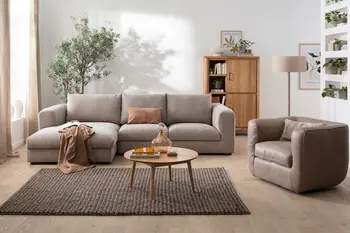 Graues Ecksofa mit einem runden Couchtisch aus Holz neben einem braunen Sessel aus Leder in kubischer Form in einem gemütlichen Wohnzimmer.