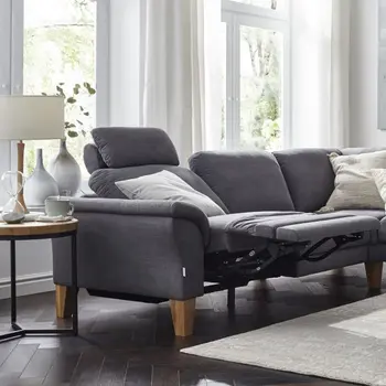 Graues Sofa, bei dem die Fußstütze ausgeklappt ist in einem gemütlich dekorierten Wohnzimmer mit Beistelltisch, Lampe und Vasen.