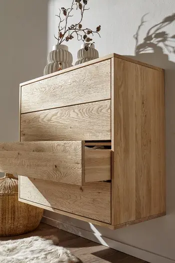 Hängende Kommode einer Garderobe mit offener Schublade in hellem Holz, dekoriert mit weißen Vasen, in einer Vase sind Blumen.