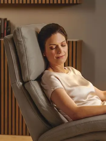 Frau sitzt mit geschlossenen Augen in einem hellbraunem Relaxsessel.