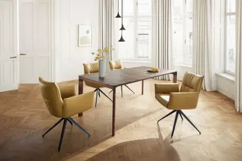 Designer Esstisch in Nussbaum mit filigranen Tischbeinen, um den Tisch stehen gelbe Armlehnstühle in einem hellen Raum.