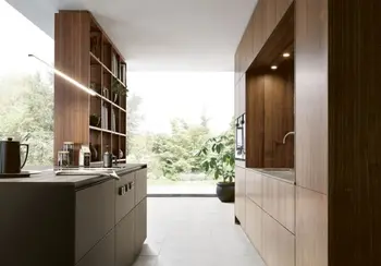 Küchenzeile mit Holzfronten in einem Loft mit großen Fensterfronten. Gegenüber steht eine Kochinsel mit integriertem Bücherregal.&nbsp;