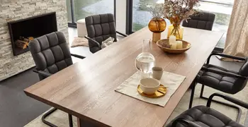 Schwarzer Freischwinger in gesteppter Retro-Optik an einem Massivholz Esstisch in einem gemütlichen Esszimmer mit Kamin und Vasen mit Trockenblumen.