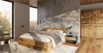 Bett aus Massivholz vor einer Wand im Beton Optik, daneben ein Kleiderschrank ebenfalls aus Massivholz in einem gemütlichen sehr hellen Schlafzimmer.