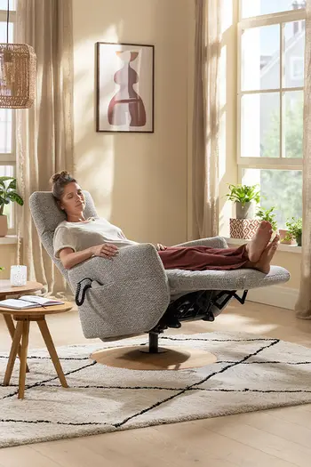 Eine Frau liegt entspannt auf einem grauen Relaxsessel mit ausgeklappter Fußstütze.