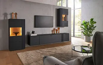Modernes Wohnzimmer mit stilvollem schwarzen Wohnwand-Set aus Holz – bestehend aus Hänge- und Standvitrinen mit integrierter LED-Beleuchtung und großem Lowboard unter einem Wand-TV, kombiniert mit eleganter Dekoration und heller Raumgestaltung.
