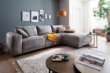 Gemütliches graues Ecksofa mit Stoffbezug, auf dem Kissen in grau, weiß und gelb sowie eine gelbe Decke liegen.