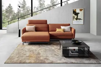 Rostrotes Ecksofa mit aufgestellter Kopfstütze in einem modernen Wohnzimmer mit großer Fensterfront und Sichtbetonwänden.