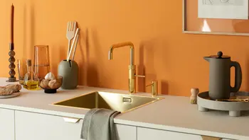 Moderne Küche mit goldener Spüle und Armatur vor orangefarbener Wand, dekoriert mit Küchenutensilien und Accessoires