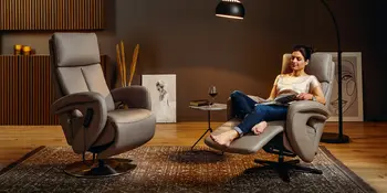 Entspannende Frau auf Relaxsessel neben weiterem Relaxsessel in gemuetlichem Wohnzimmer.