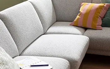 Nahaufnahme eines modernen Ecksofas in hellem Stoff mit weicher Polsterung und farbigen Zierkissen – stilvolle Wohnlandschaft für gemütliches Sitzen im Wohnzimmer.