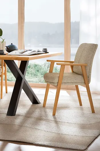 Ein Armlehnstuhl mit Gestell aus Wildeiche steht neben Esstisch mit passender Tischplatte und schwarzem Metallgestell.