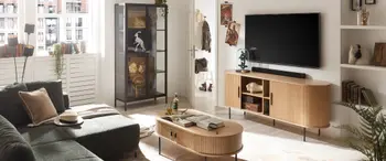 Ein gemütliches Wohnzimmer mit Schlafsofa, Zweisitzer und Couchtisch, angeordnet um einen Fernseher auf einem Entertainment-Center. Der Innenraum ist mit Regalen dekoriert und verfügt über ein Fenster, das viel Tageslicht in den Raum lässt.