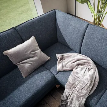 Sitzfläche eines blauen Ecksofas ohne Kopfstützen, auf dem ein helles Kissen und eine Decke mit hell-dunklem Muster liegt.