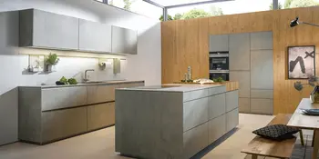 Inselkueche im Beton-Look mit eingebauter Herdplatte und Holzwand mit Einbaugeraeten.