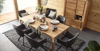 Gemütliches Esszimmer mit einem Esstisch und Highboard aus Massivholz, grauen Schalenstühlen um den Esstisch, der schön gedeckt ist.