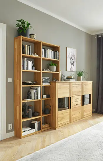 Offenes Bücherregal mit passendem Sideboard aus massiver Eiche – stilvolle Wohnwand-Kombination mit viel Stauraum, Dekorationen und modernen Accessoires vor grauer Wand in einem hellen Wohnzimmer mit Parkettboden