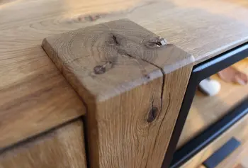 Detailaufnahme einer massiven Holzecke mit sichtbarer natürlicher Maserung und Rissen auf einem Möbelstück aus Eichenholz.