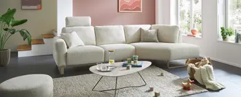 Modernes Ecksofa in hellem Stoffbezug mit verstellbarer Kopfstütze, dekorativen Kissen und stilvollem Couchtisch – familienfreundliches Wohnzimmer mit gemütlicher Spielatmosphäre.