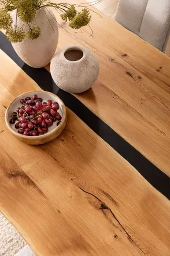 Tischplatte aus Massivholz mit schwarzem Epoxidharz in der Mitte, auf dem Tisch stehen 2 graue Vasen und eine Schale mit Weintrauben.