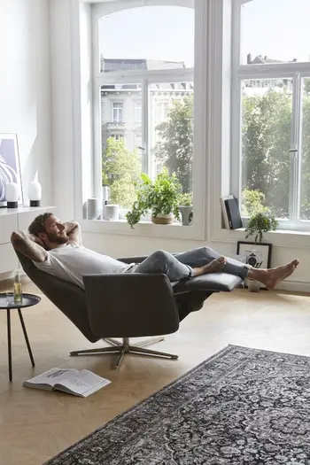 Mann liegt entspannt auf einem schwarzen Relaxsessel, bei dem die Rückenlehne nach unten geklappt ist und die Fußstütze nach oben.
