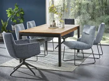 Graue Polsterstühle mit und ohne Armlehne mit schwarzem Metallgestell, die um einen Esszimmertisch aus Holz mit schwarzem Metallgestell stehen auf dem eine Blumenvase und Kerzen stehen.