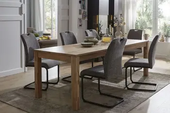 Massivholz Esstisch mit Holzbeinen, um den graue Freischwinger Stühle mit schwarzem Gestell stehen in einem hellen Raum.