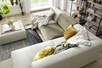 Modernes Ecksofa in beige, mit einer Sitzfläche in grün, dekoriert mit mehreren Kissen in gelb, grün und weiß in einem hellen Raum.