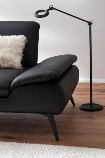 Schwarzes Designersofa aus Leder mit filigranen schwarzen Beinen und einem weißen Fellkissen auf der Sitzfläche.