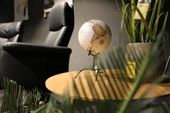 Dekorative Wohnzimmerszene mit schwarzem Ledersessel, einem kleinen runden Holztisch mit Globus und grünem Pflanzendekor im Vordergrund.