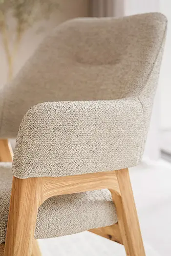 Detailbild von Armlehne eins Esszimmerstuhls im Retro-Look in beigem Stoff.