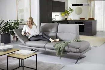 Eine Frau liegt auf einem grauen Ledersofa mit rollbaren Armlehnen.