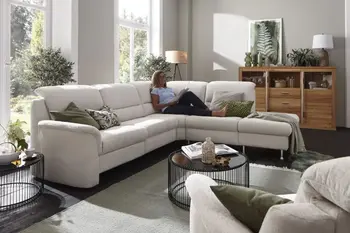 Beiges Ecksofa mit silbernen Füßen und umgeklappten Kopfstützenauf dem eine Frau entspannt liegt und zufrieden lächelt.