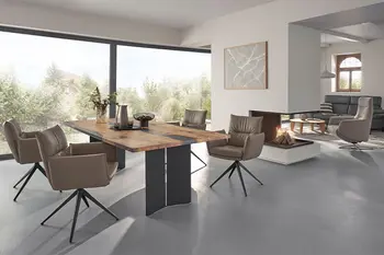 Halboffener Essbereich in einem sanierten Bauernhaus mit Massivholz Esstisch und drehbaren grauen Armlehnstühlen. 