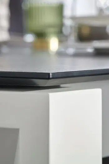 Ecke eines Esstisches mit schwarzer Tischplatte und weißem Gestell.