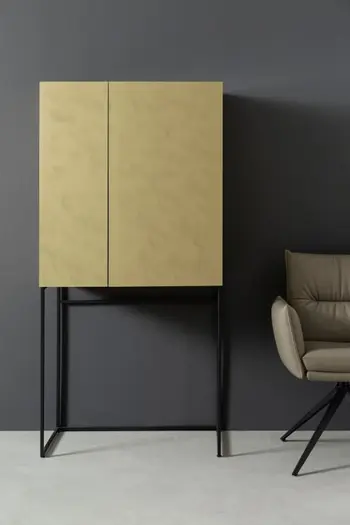 Goldener Barschrank mit schwarzem Metallgestell der vor einer grauen Wand steht.