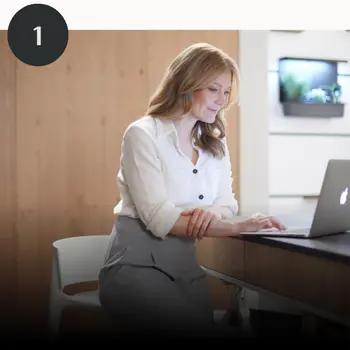Frau sitzt in einer Holzküche vor dem Laptop.