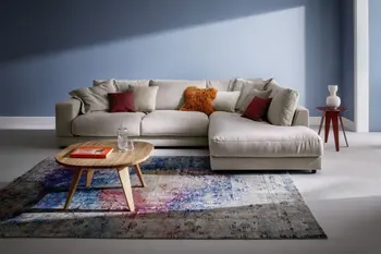 Wohnzimmer mit blauen Wänden, beigem Ecksofa, buntem Teppich und Beistelltisch aus Holz.