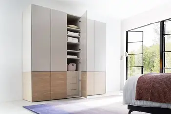 Moderner weißer Kleiderschrank, der am unteren Teil Holzelemente hat und fünf Türen hat, die dritte Türe ist geöffnet und man sieht Regalböden im oberen Teil und Schubladen im unteren Teil.