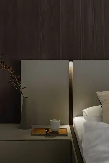 Graue Nachtkonsole, die am Bett befestigt ist, auf der Konsole stehen eine Vase und eine Tasse auf einem Tablett, am Bettrahmen ist eine Beleuchtung integriert.