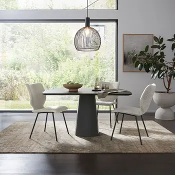 Dunkler Design Esstisch mit rundem Fuß und zwei weißen Schalenstühlen in einem hellen Esszimmer.