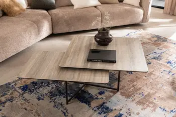 Moderner beiger Keramik Couchtisch mit schwarzem Gestell und zwei Tischplatten, die schräg versetzt übereinander angeordnet sind.