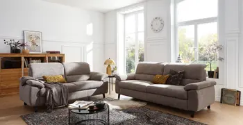 Zwei gemütliche graue Sofagarnituren mit hoher Rückenlehne in einem hellen Raum.