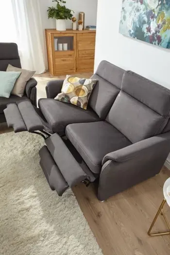 Graues Sofa mit ausgeklappten Fußlehnen und einem gemusterten Kissen auf der Sitzfläche.