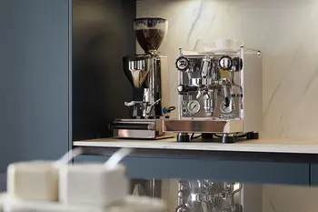 Kaffeemühle und Kaffeemaschine in einer Design Küche mit heller Arbeitsplatte und blauen matten Schränken.