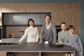 Glückliche Familie, die vor einer modernen Küche mit Holz und grauen Elementen steht.